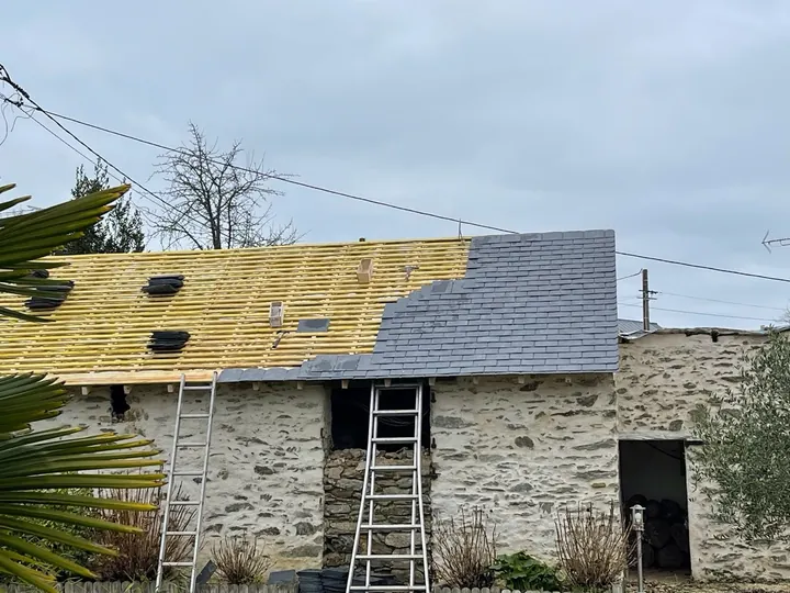 Liteaux apparents et couverture en ardoise en cours de pose sur un bâtiment en pierre.