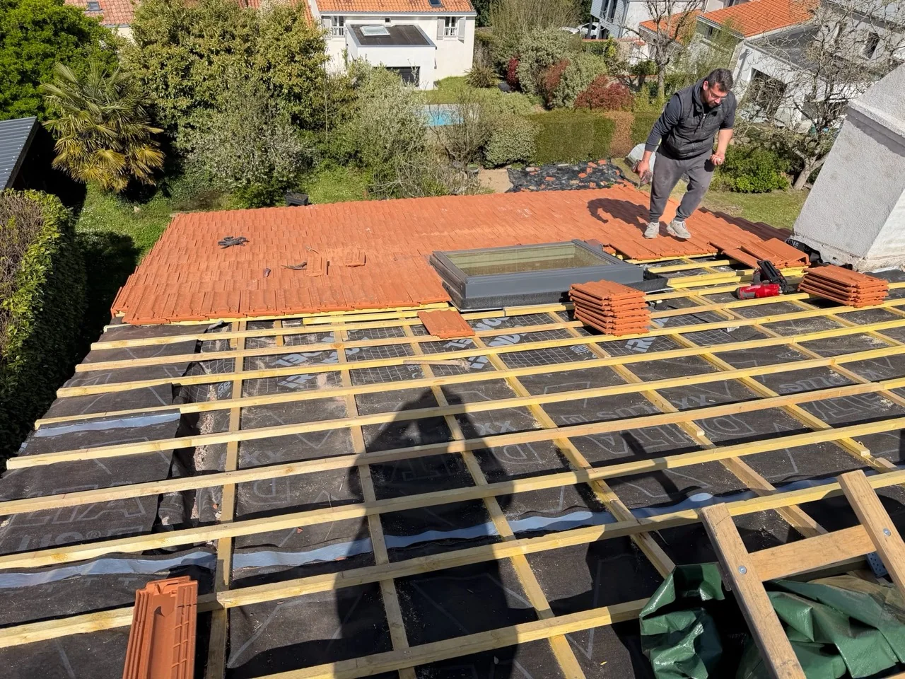 Liteaux et écran de sous-toiture visibles autour d’une fenêtre de toit, avec pose de tuiles en cours.