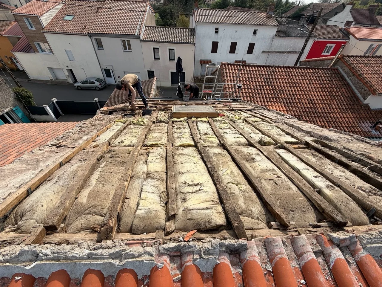 Pièces de bois et isolant apparents après dépose de la couverture, autour d’une fenêtre de toit.