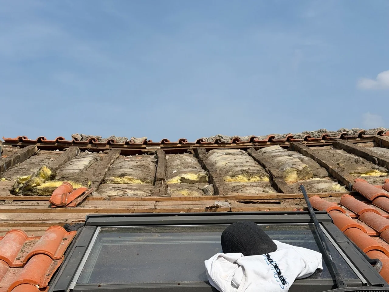 Détail d’une fenêtre de toit pendant les travaux, avec bois, isolant et tuiles visibles.